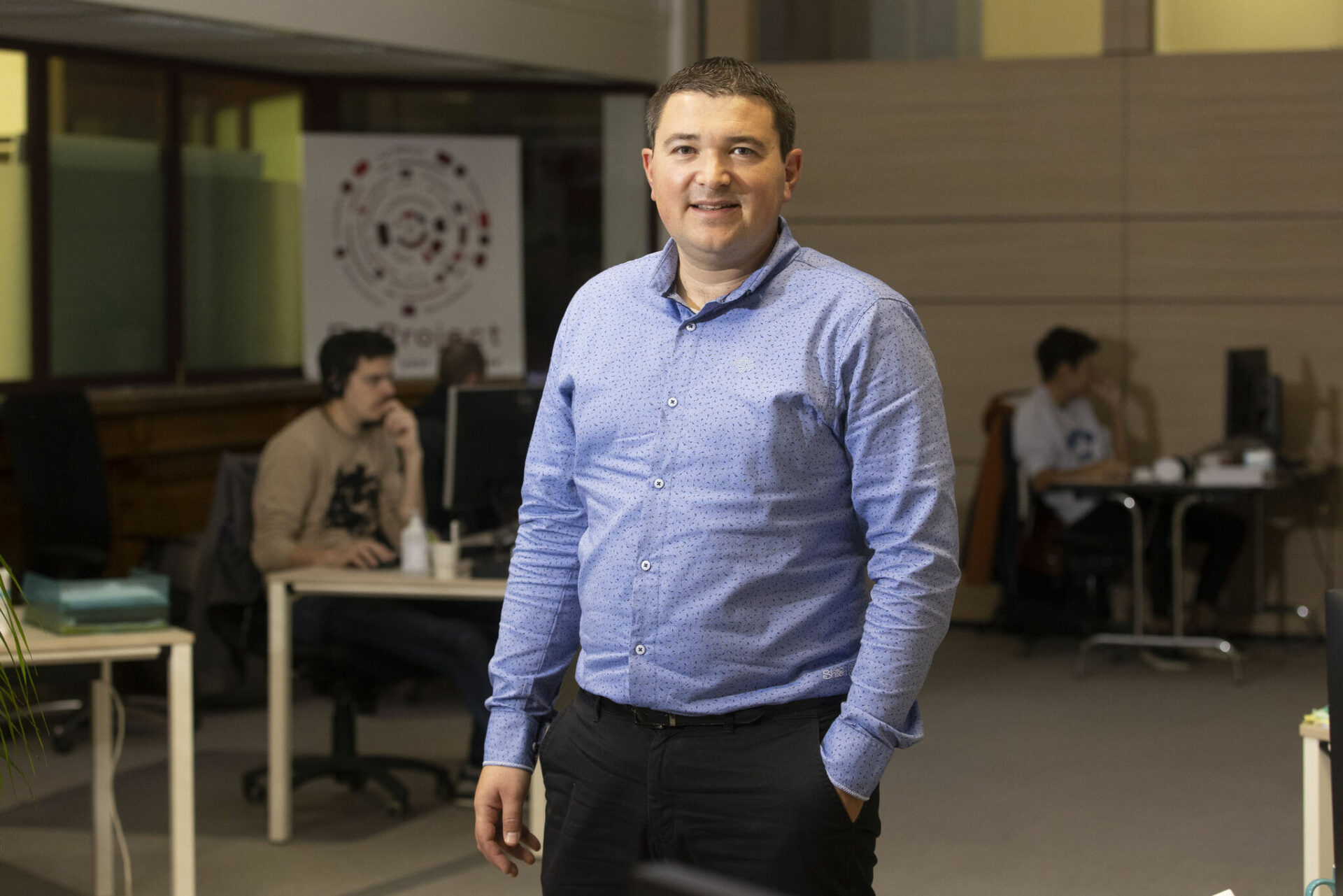 Portait de Julien Virgili souriant en chemise devant ses équipes